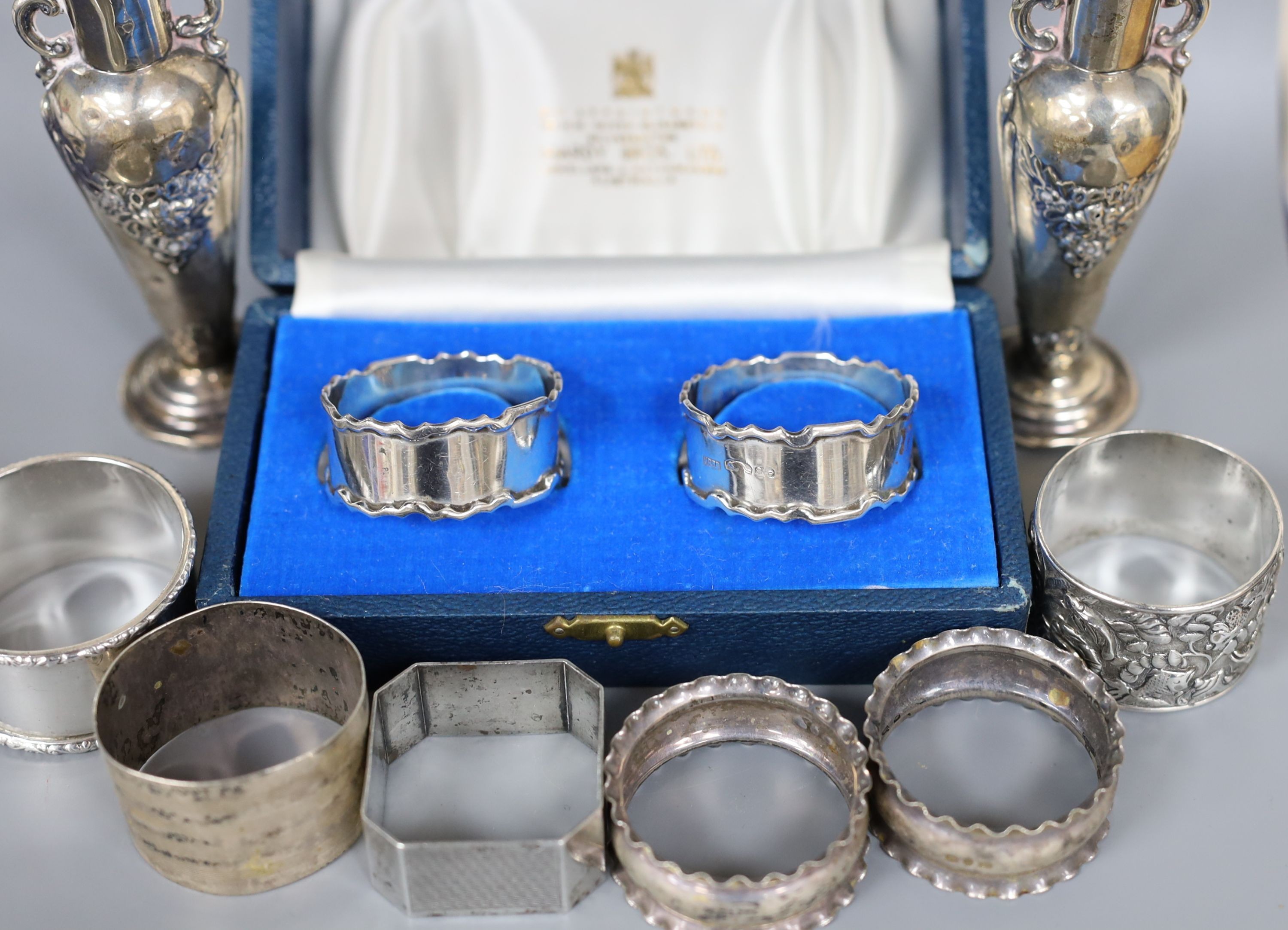 A cased pair of silver napkin rings, five others including one white metal and a two small silver vases, weighted.